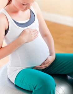 Young pregnant woman touching her belly sitting on a fitness bal